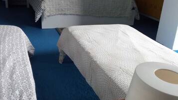 A hotel room with two beds, a wicker side table with a lamp, and a blue carpet.