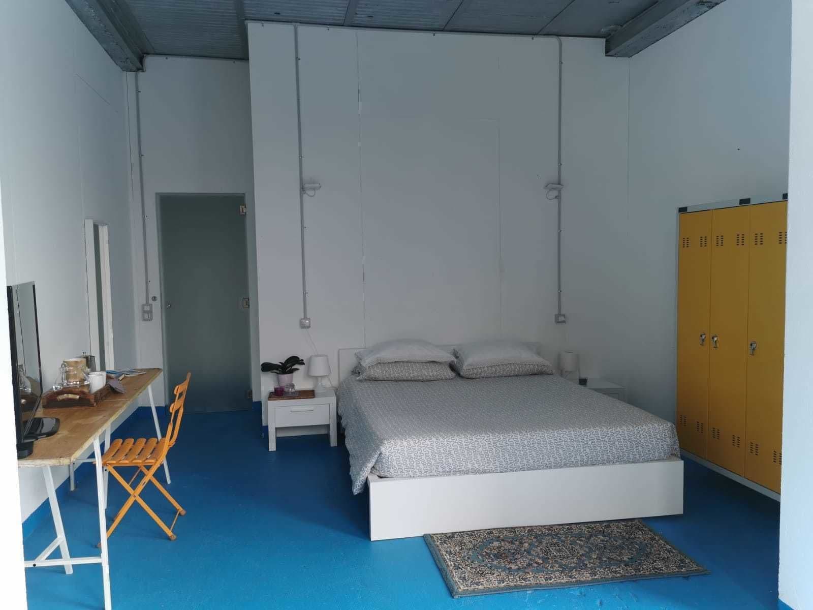 A bedroom with a bed, a desk, a chair, a wardrobe, and a small rug.