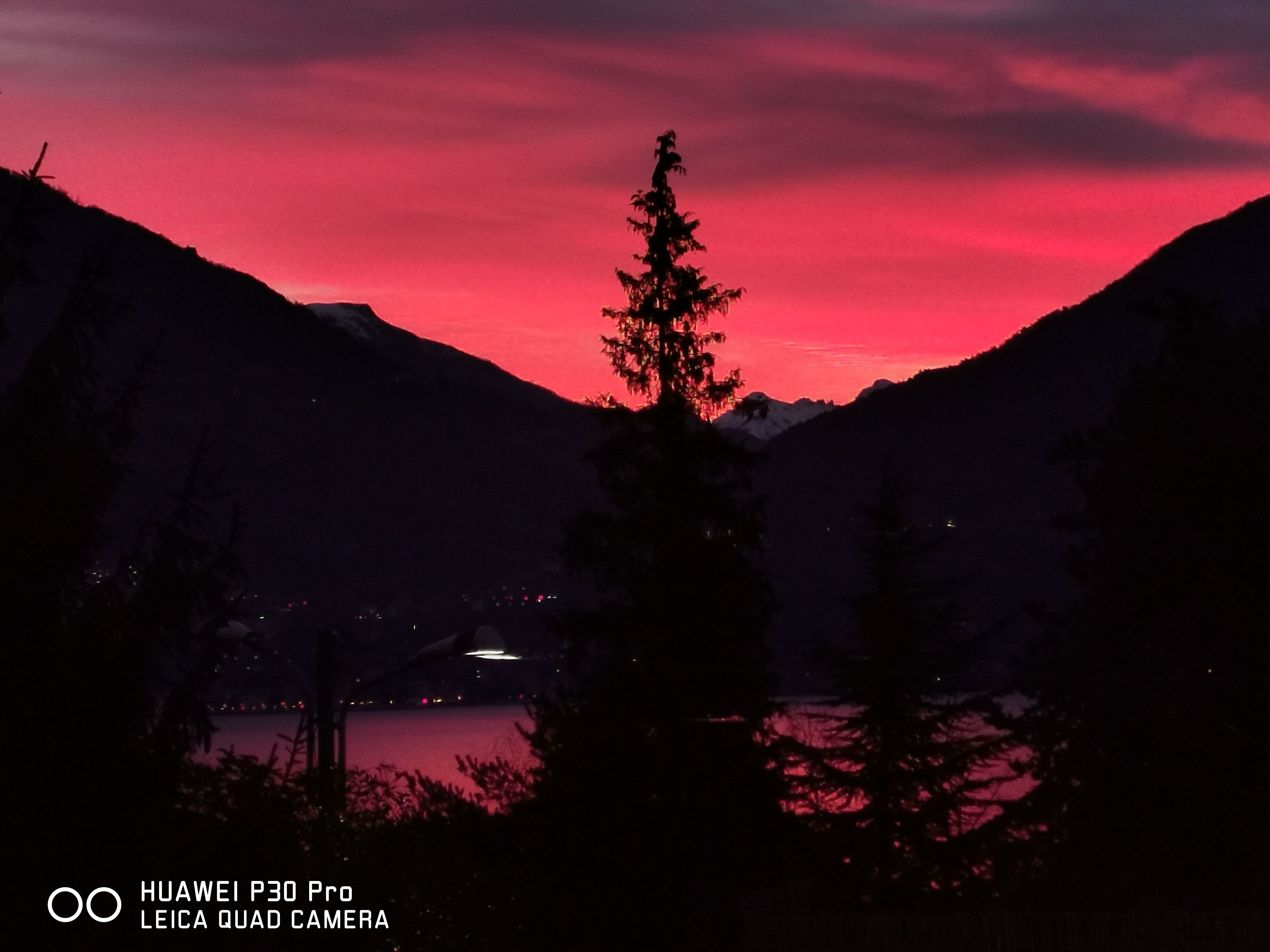 A mountain landscape with a lake at sunset, featuring a prominent tree in the foreground.