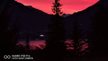 A mountain landscape with a lake at sunset, featuring a prominent tree in the foreground.