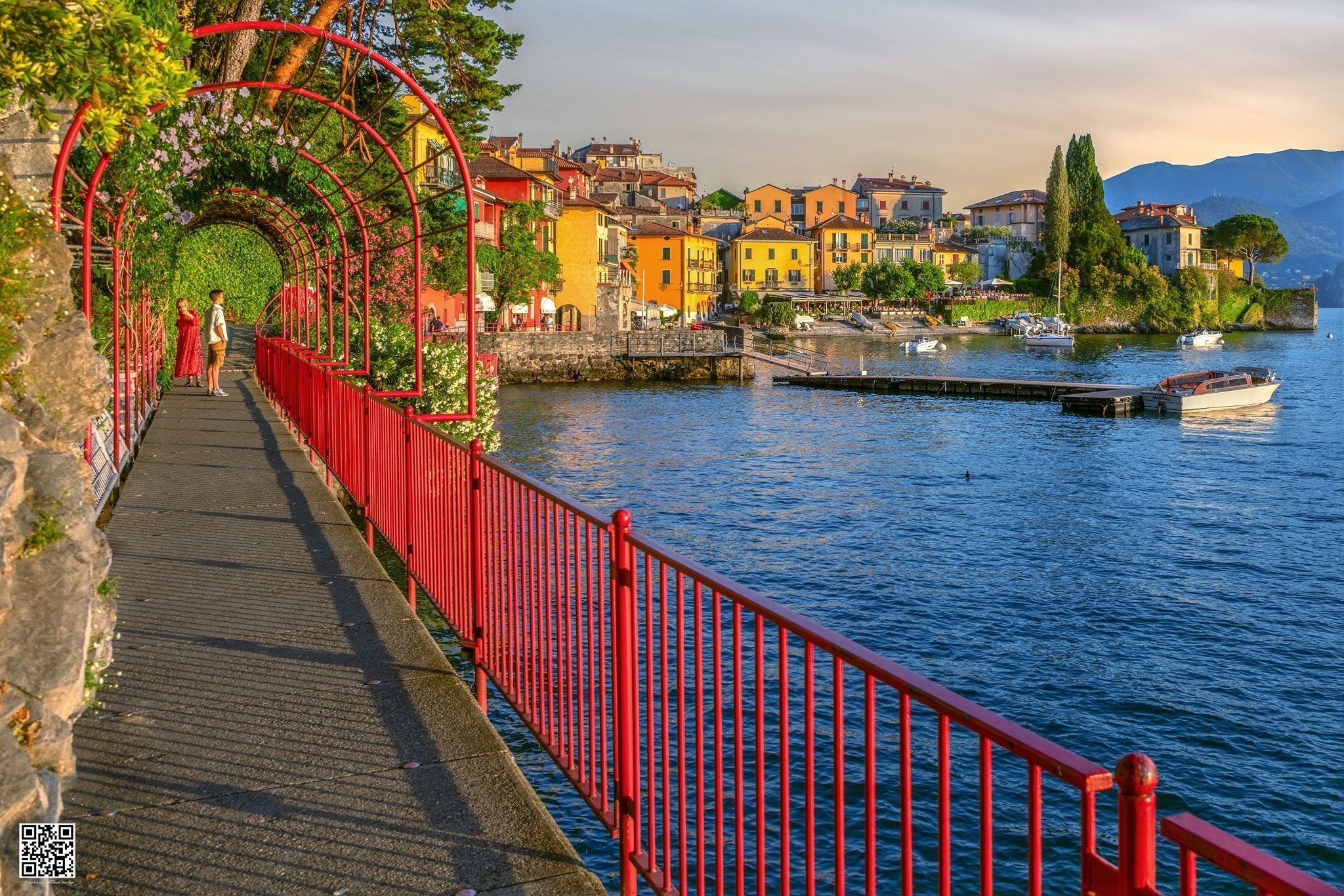 Eine rote Fußgängerbrücke über einem Gewässer, im Hintergrund bunte Gebäude.