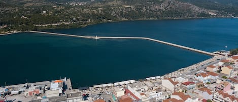 Vista aérea de un pueblo costero con un puerto deportivo, edificios con techos de tejas rojas y montañas al fondo.