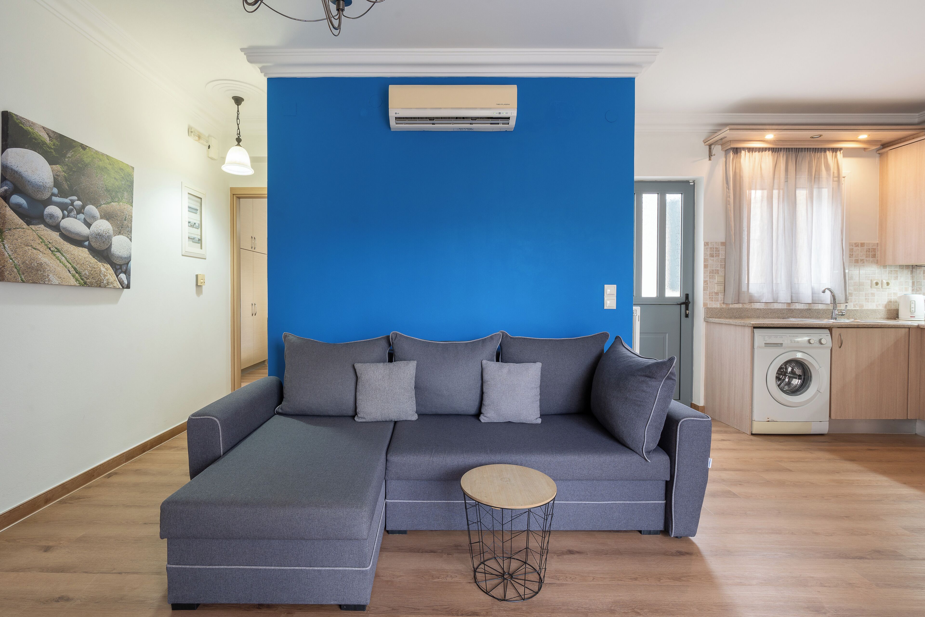 A modern living room with a sectional sofa, a round coffee table, and a washing machine in the background.
