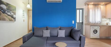 A modern living room with a sectional sofa, a round coffee table, and a washing machine in the background.