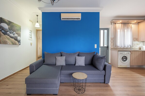 A modern living room with a sectional sofa, a round coffee table, and a washing machine in the background. - Elegant Living (Kefalonia)