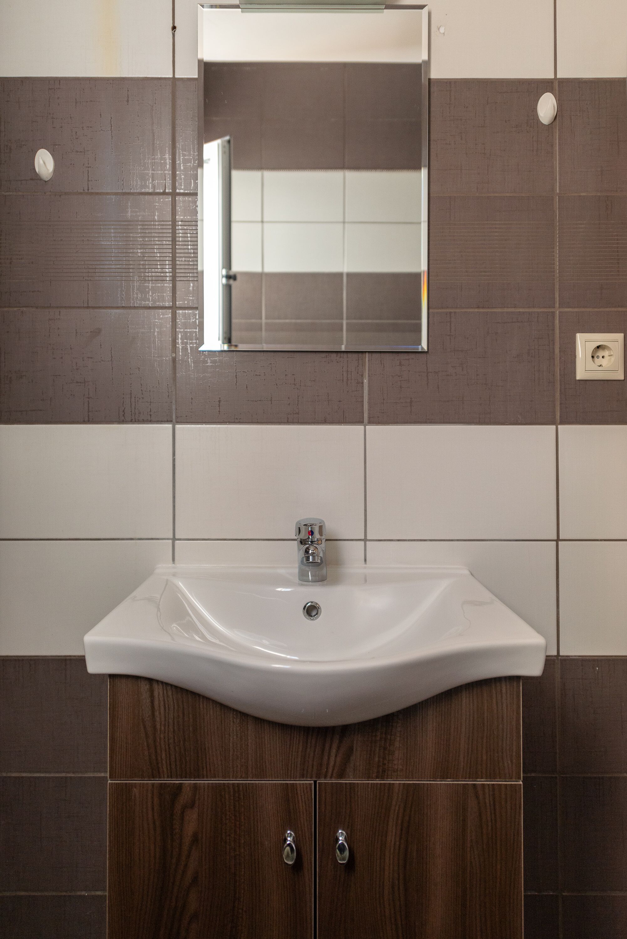 Un baño con lavamanos blanco, mueble de madera y espejo encima.