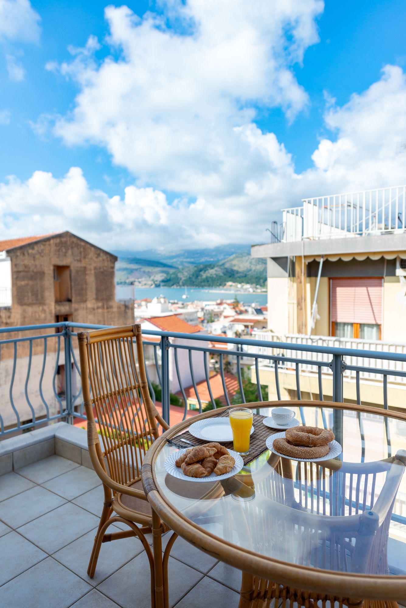 Ein Balkon mit Frühstückstisch, auf dem Croissants und Orangensaft stehen, mit Blick auf eine Küstenstadt.