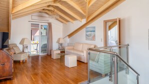 A spacious living room with wooden beams, a glass staircase, and a view to the outside.
