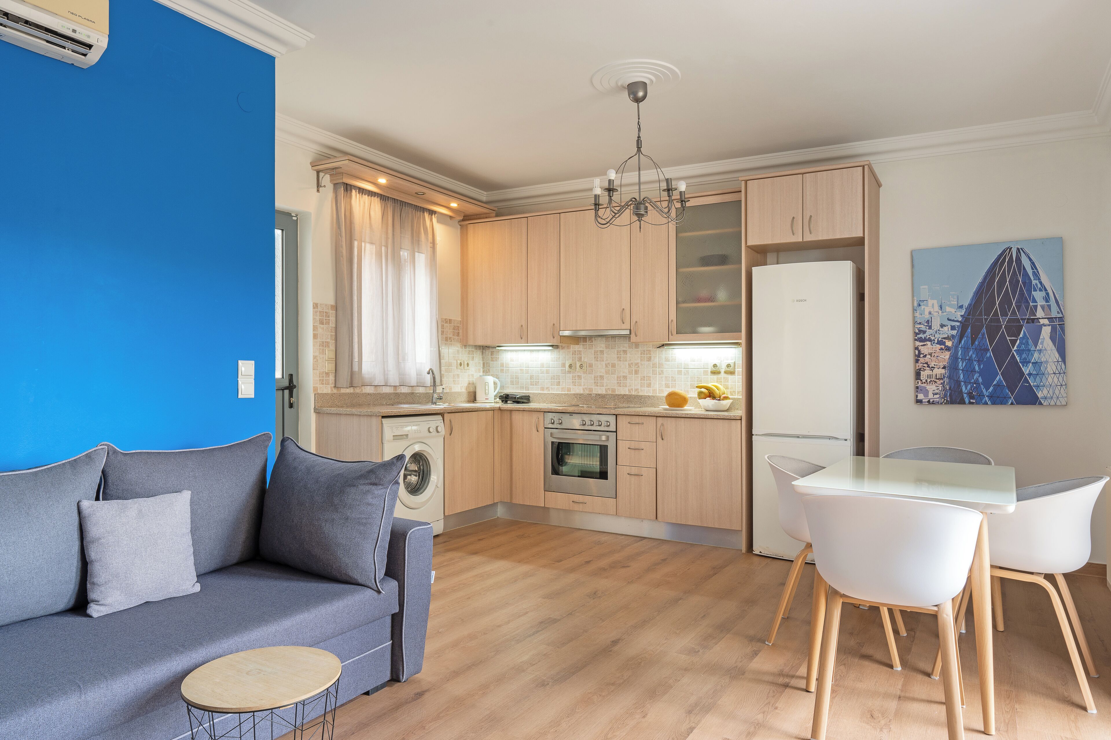 A compact kitchen with a washing machine, a dining area with a table and chairs, and a sofa.