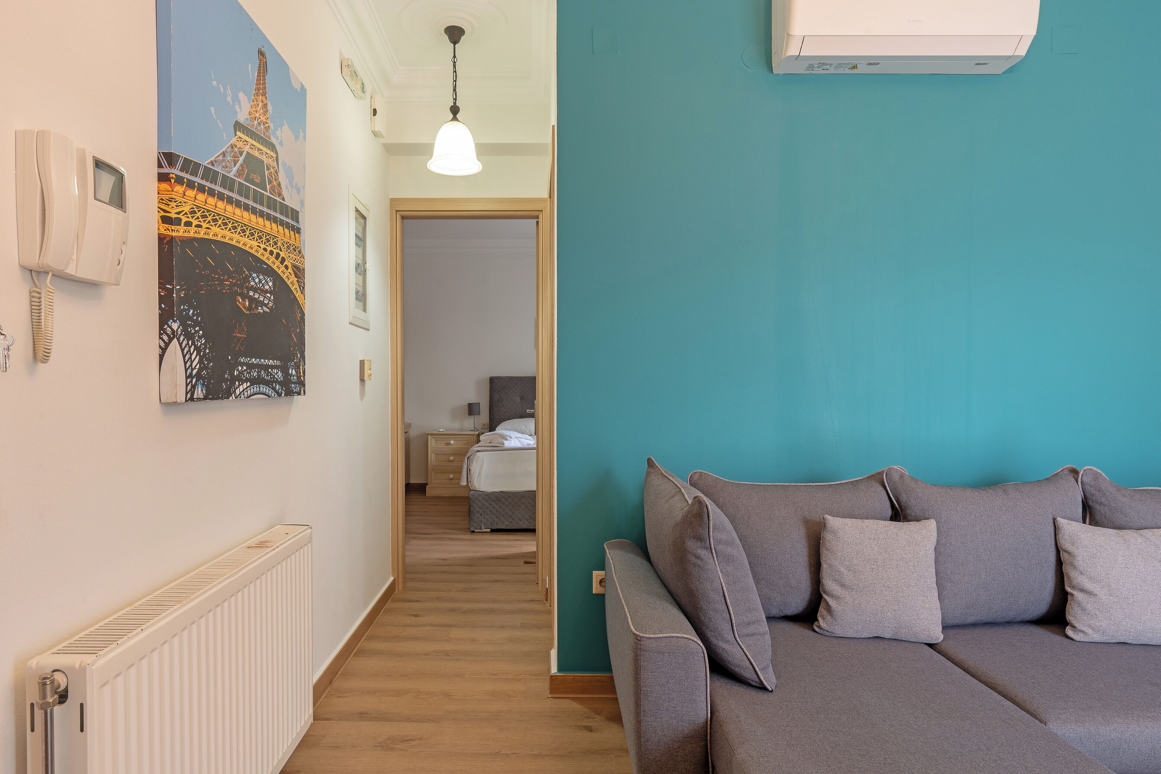 Ein Hotelzimmer mit einer wandfarbenen Wand in Türkis, einem grauen Sofa, einem weißen Heizkörper und einem Gemälde des Eiffelturms.