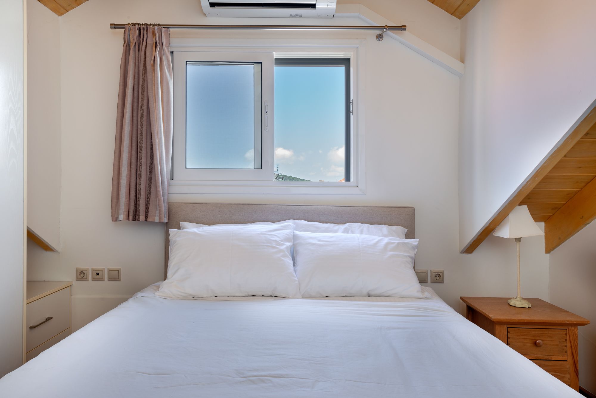 Une chambre à coucher avec un lit, une fenêtre, une table de chevet et une lampe.
