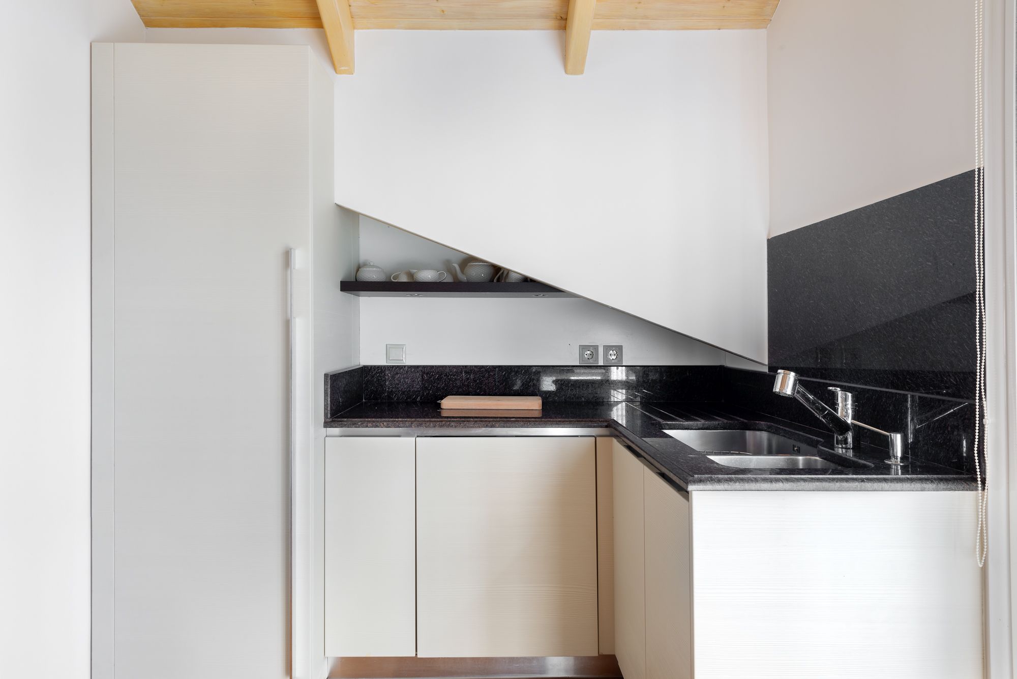 A compact kitchen with white cabinets, a black countertop, and a stainless steel sink.