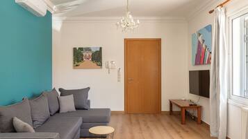 Una sala de estar con un sofá gris, una mesita redonda, una puerta de madera y un cuadro en la pared.