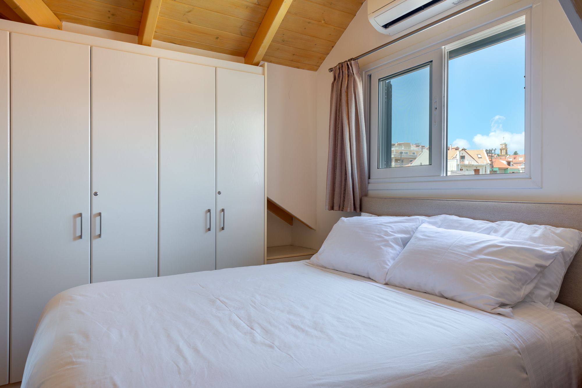 A bedroom with a bed, white wardrobe, and a window with a view of buildings.