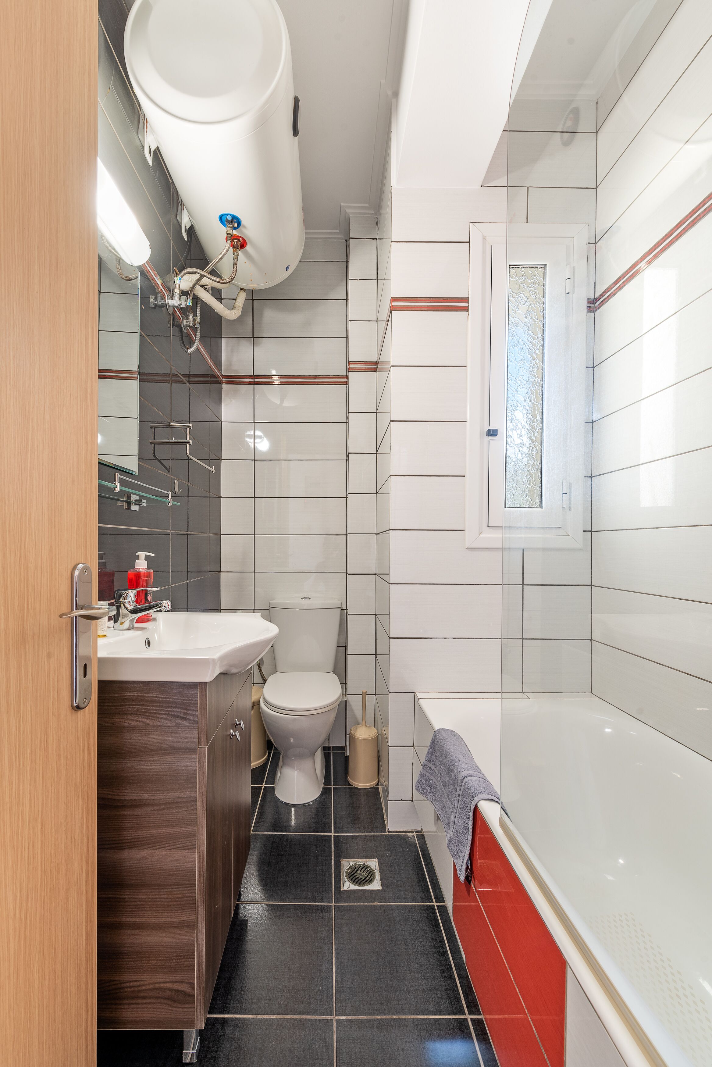Un baño moderno con inodoro blanco, lavamanos con espejo, bañera y ventana.
