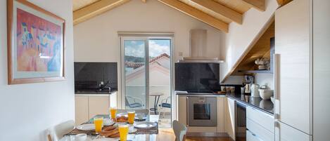 A modern kitchen with wooden beams, a dining area with breakfast set, and a view of the outside.