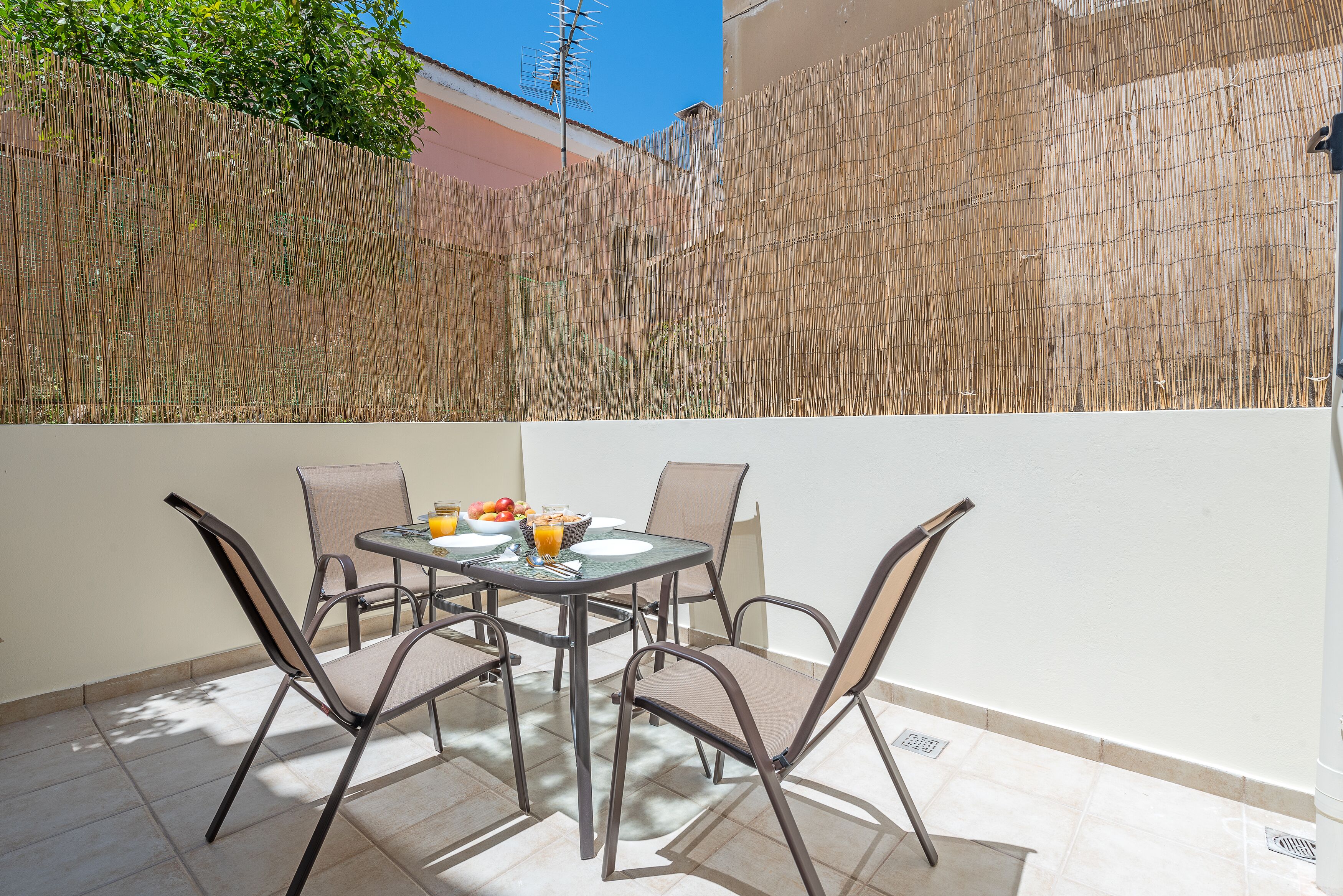 A patio with a table set for two, surrounded by chairs, and a bamboo fence in the background.