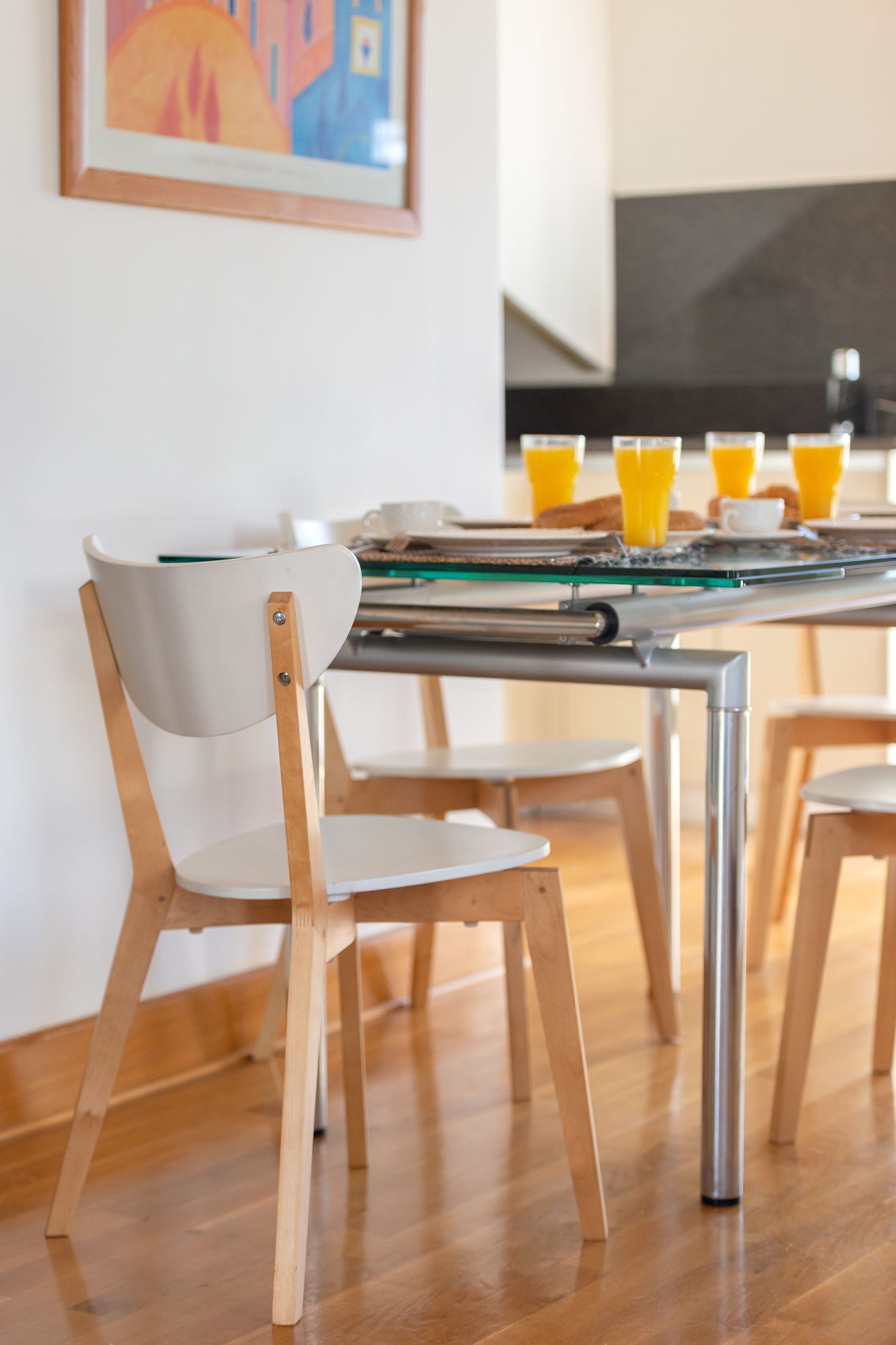 Un comedor con una mesa de vidrio, sillas de madera y una disposición para el desayuno con vasos de jugo de naranja.