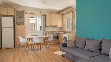 Una cocina moderna con armarios de madera, un comedor con mesa y sillas blancas, un sofá gris y una lavadora.
