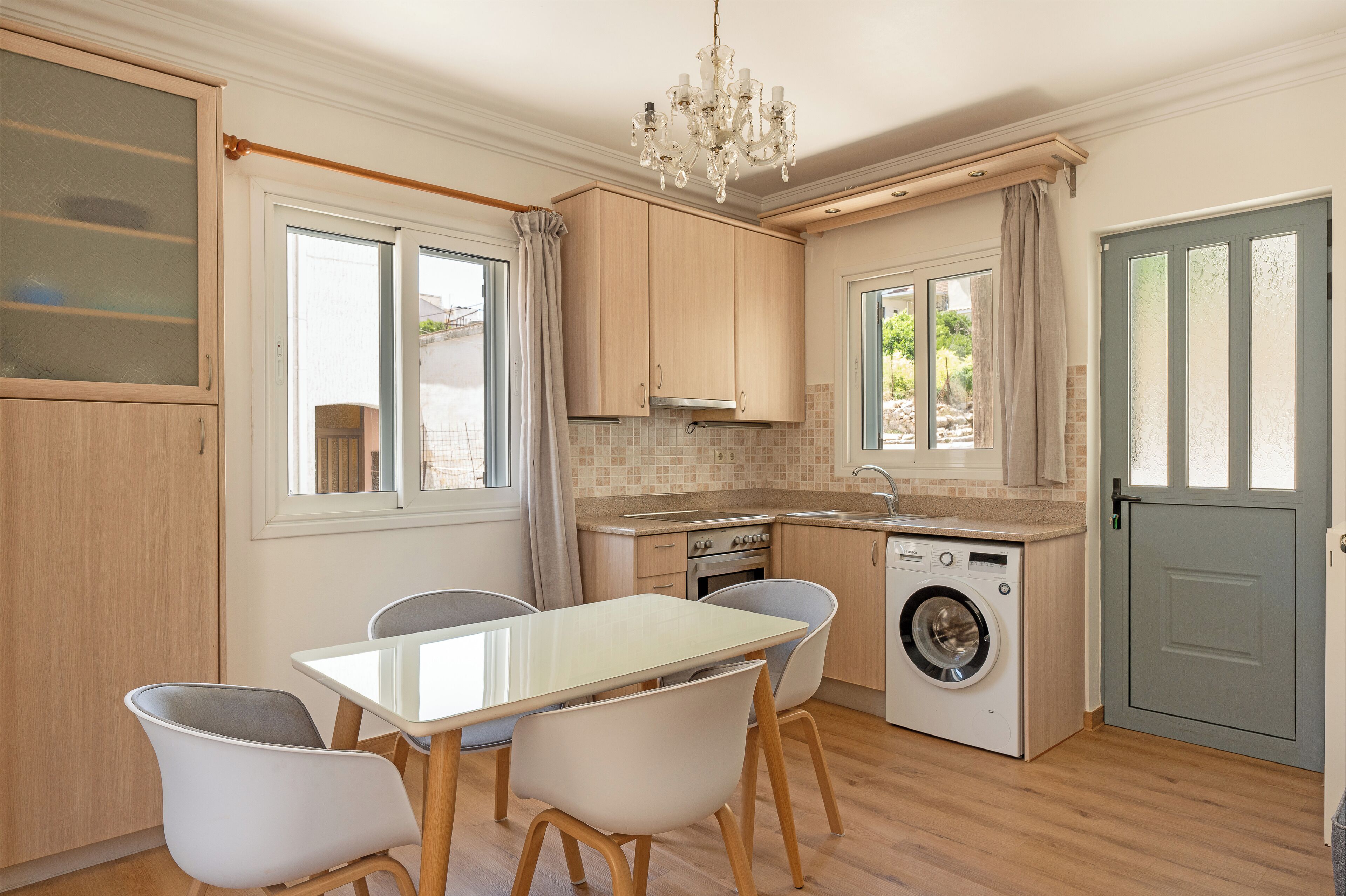 A compact kitchen with a dining area, a washing machine, and a chandelier.