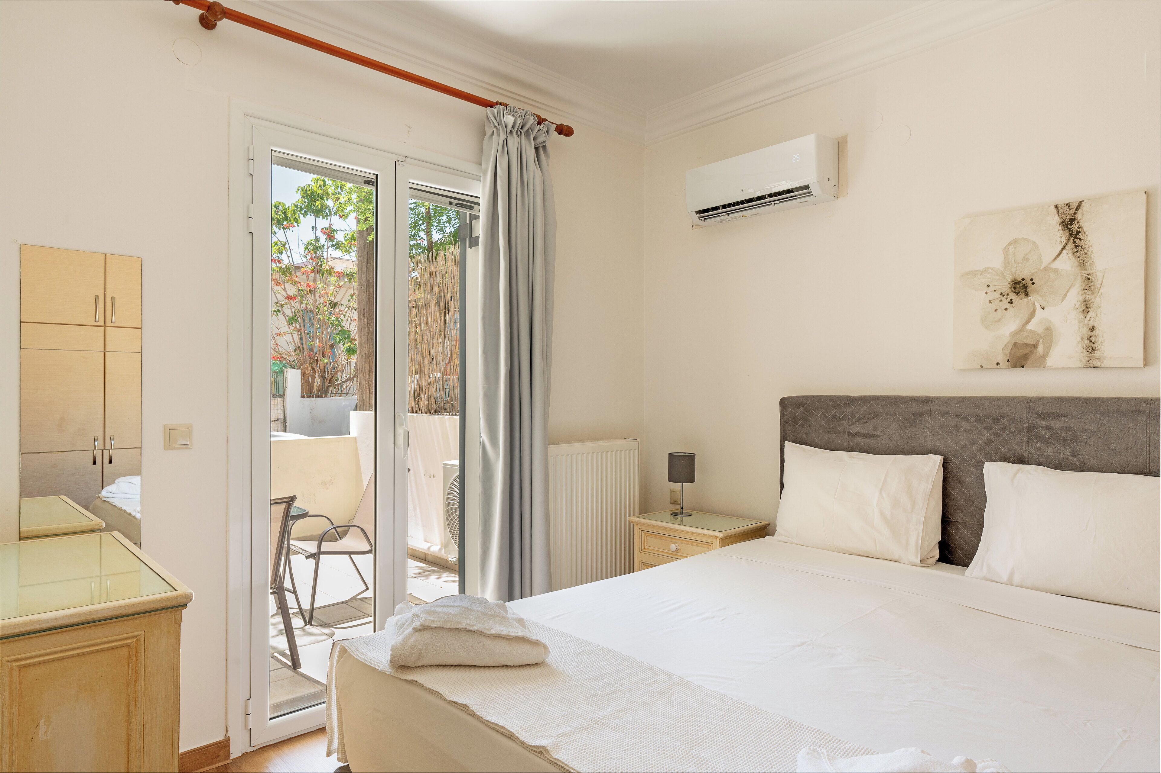 A bedroom with a bed, bedside table, lamp, and an air conditioning unit on the wall.