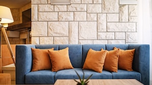 A blue sofa with four orange cushions against a stone wall. - Hotel Haliaetum - San Simon Resort (Izola)