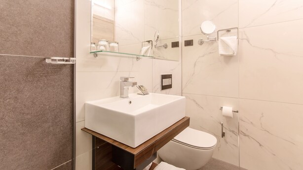 A modern bathroom with a white sink, mirror, and toilet. - Hotel Haliaetum - San Simon Resort (Izola)