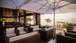 A covered outdoor seating area with wicker furniture and a view of the sea. - Hotel Haliaetum - San Simon Resort (Izola)