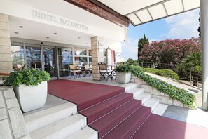 A hotel entrance with a red carpet, outdoor seating, and a view of pink flowers. - Hotel Haliaetum - San Simon Resort (Izola)