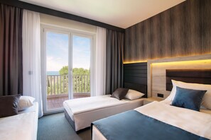 A hotel room with two beds, a balcony, and a view of greenery. - Hotel Haliaetum - San Simon Resort (Izola)