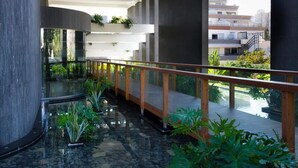 Un jardin intérieur moderne, doté d’une passerelle en verre, entouré de verdure et agrémenté d’un élément aquatique.
