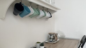 A dining area with a wooden table, chairs, and a shelf above holding kitchen utensils and glass jars. - La Dimora delle Muse (Catania)