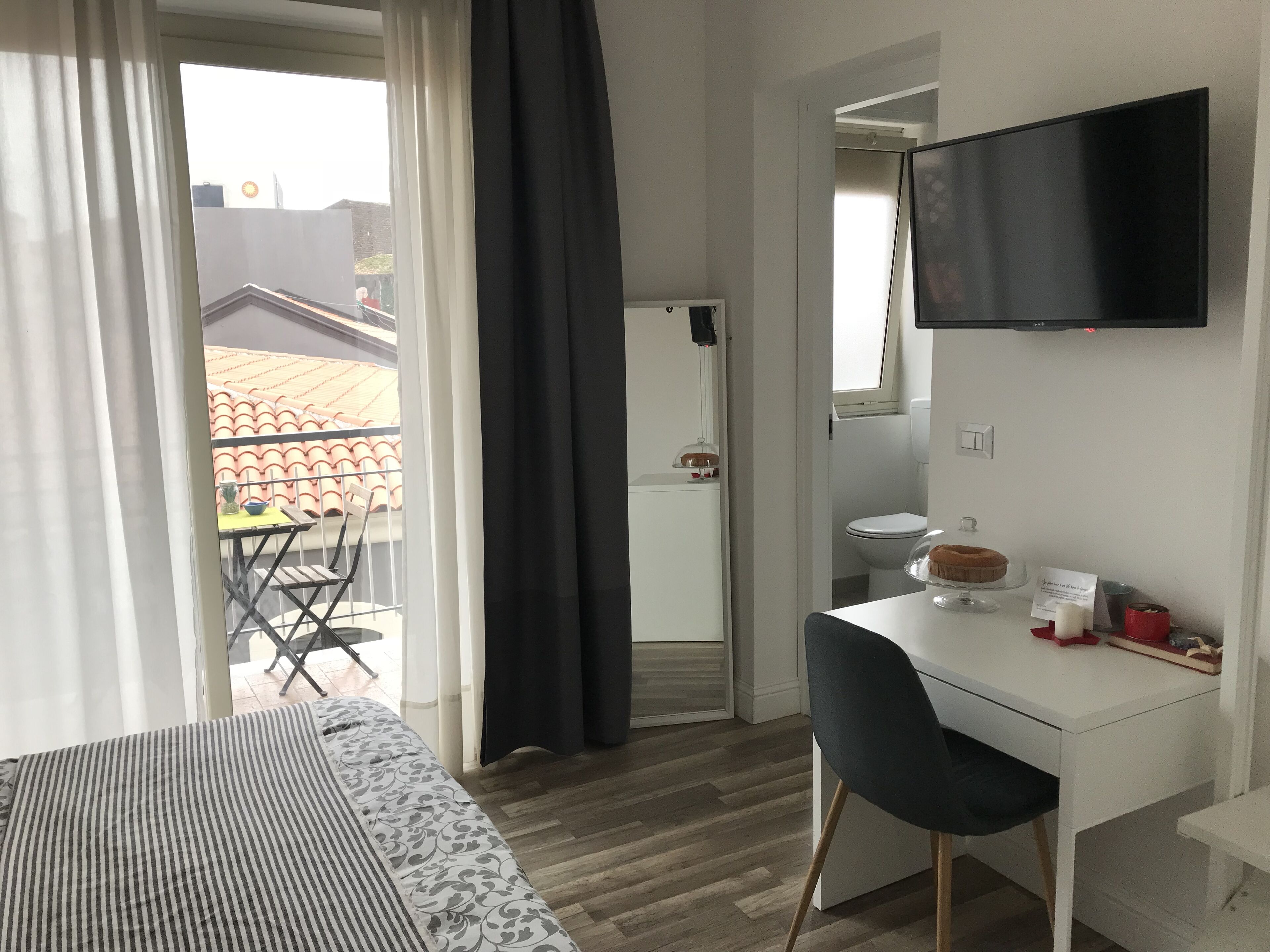 Et hotelværelse med seng, skrivebord, stol, fjernsyn og en balkon med bord og stole.