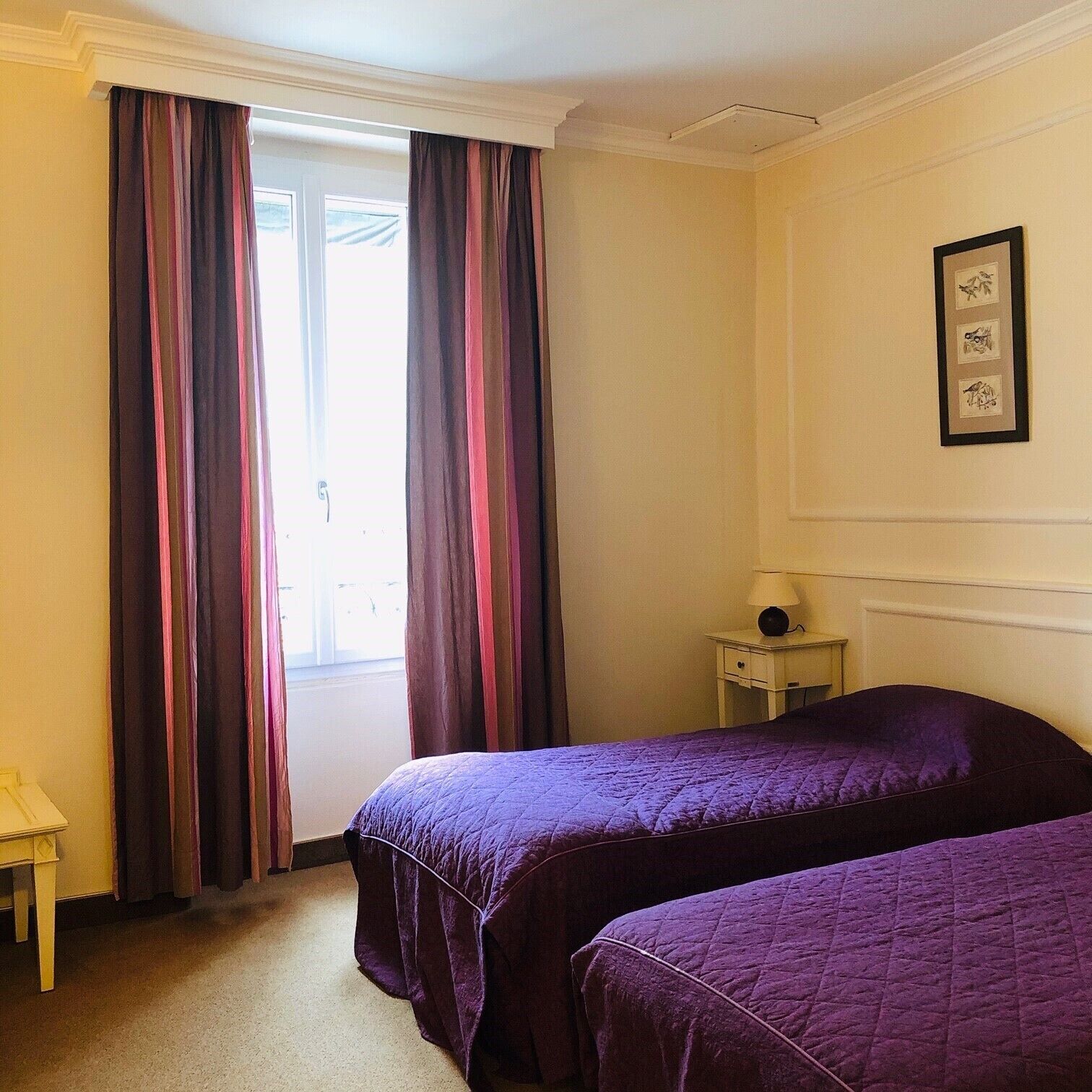 Une chambre avec deux lits, une petite table, une lampe et une fenêtre avec des rideaux.
