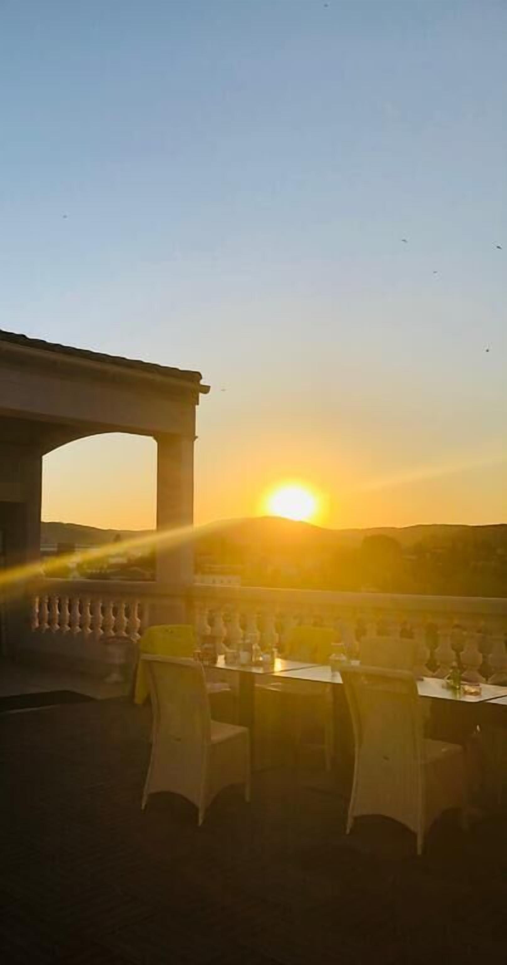 Un'area pranzo all'aperto con tavoli e sedie, un pergolato e un tramonto sullo sfondo.