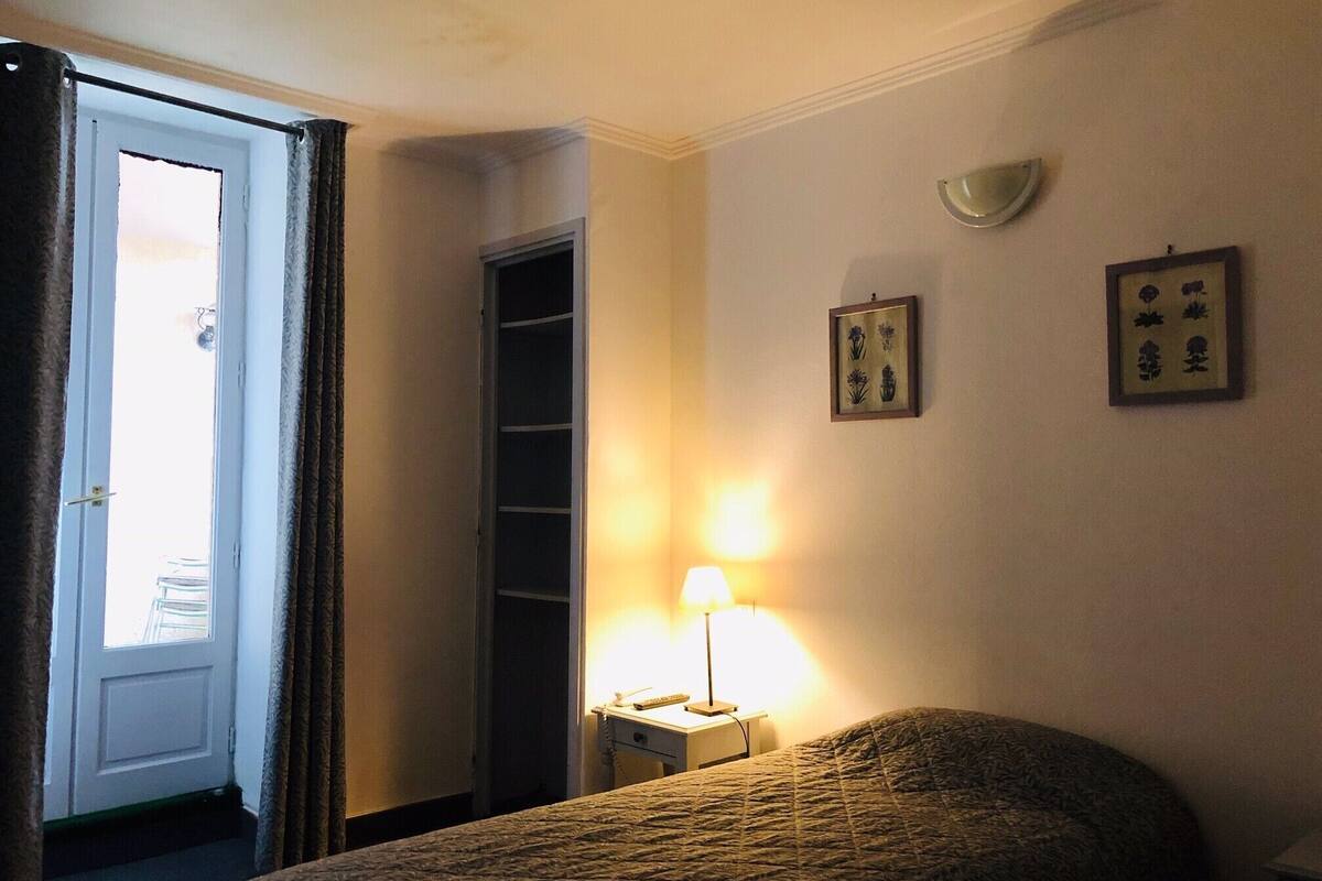 A hotel room with a bed, a nightstand with a lamp, a door, and a wall with framed pictures.