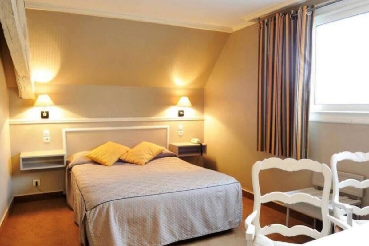 A bedroom with a bed, two bedside lamps, a chair, and a window with curtains.