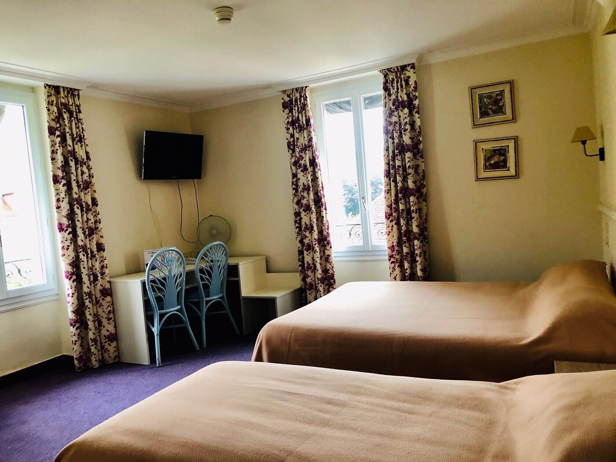 Une chambre d’hôtel avec deux lits, un bureau avec des chaises, un téléviseur fixé au mur et des rideaux.