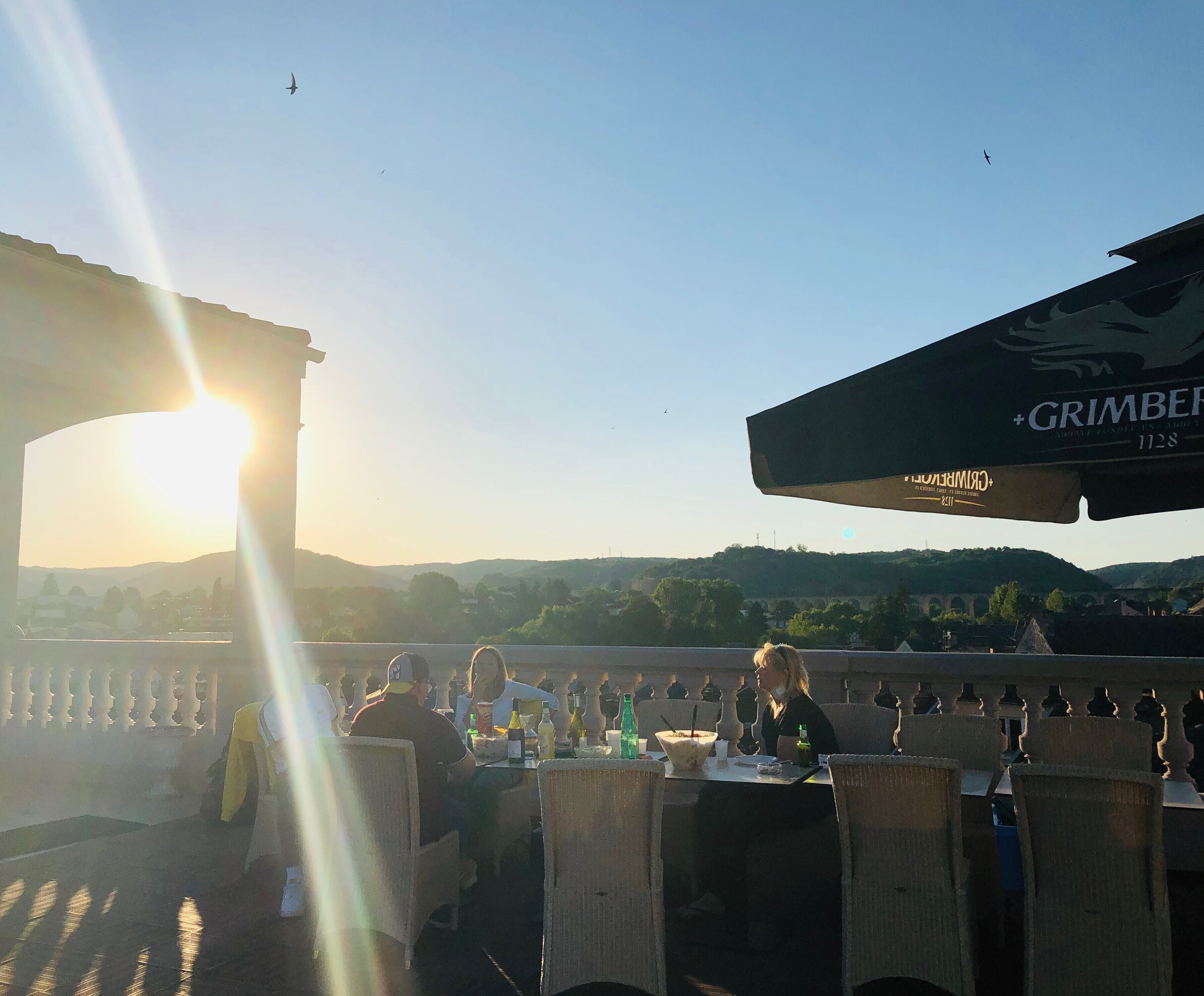 En udendørs spiseplads med borde og stole, en klar himmel og fjerne bakker.