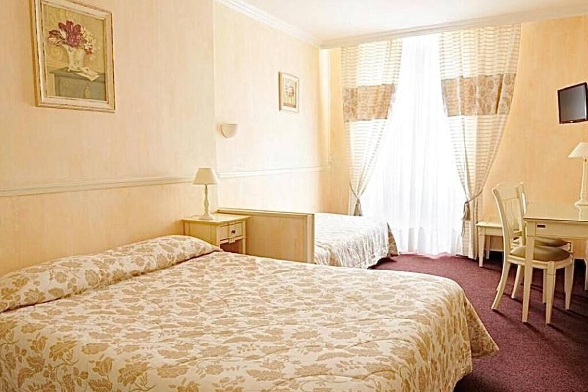 A hotel room with two beds, a desk, a chair, and a TV.