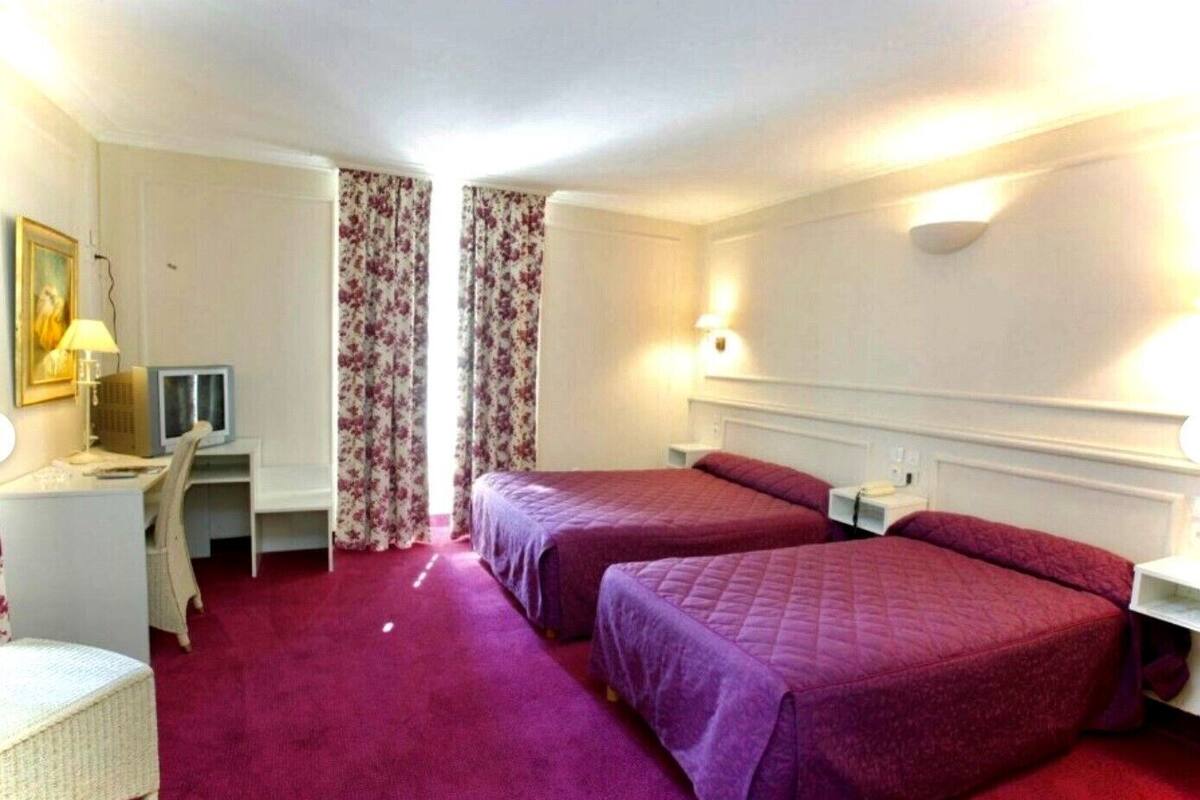 A hotel room with two beds, a desk with a computer, a chair, and a small table.