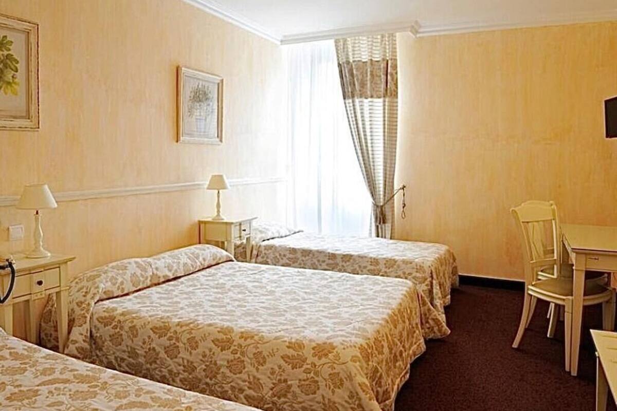 A hotel room with three single beds, a desk, and a chair.