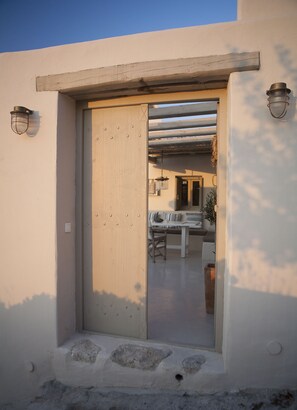 Une entrée moderne avec une porte en bois, un petit seuil et un espace extérieur abrité avec des sièges, visible à travers la porte.