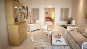 Un salon chaleureux avec un canapé, une table à manger et un meuble. Au fond, on aperçoit un lit, une fenêtre et une lampe.