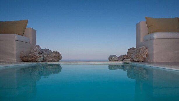 Une piscine offrant une vue dégagée sur l’océan, entourée de rochers et de chaises de couleur beige.