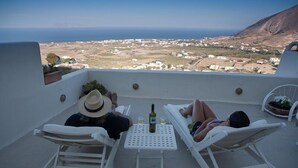 Une terrasse avec deux fauteuils blancs, une petite table sur laquelle se trouvent une bouteille et des verres, et une vue sur un paysage côtier.