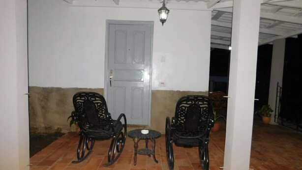 Un espace extérieur abrité, avec deux chaises et une petite table, une porte et un luminaire suspendu.