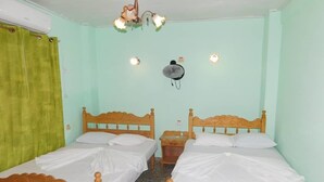 Une chambre avec deux lits en bois, un ventilateur de plafond et un radiateur fixé au mur.