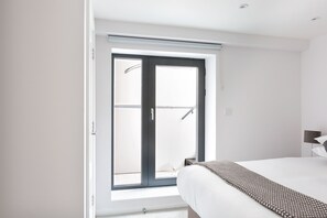 A bedroom with a large window, a bed, and a nightstand.