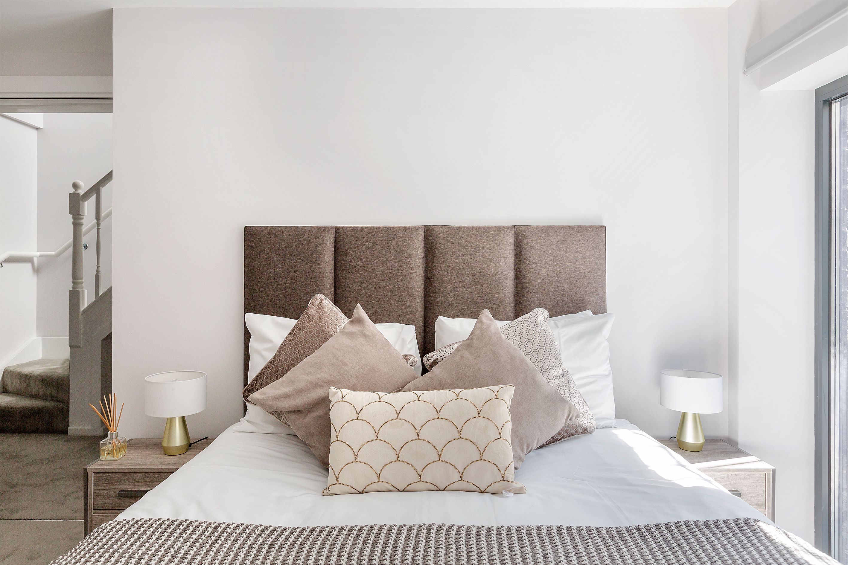 A neatly arranged bedroom with a bed, pillows, bedside tables, and a lamp.